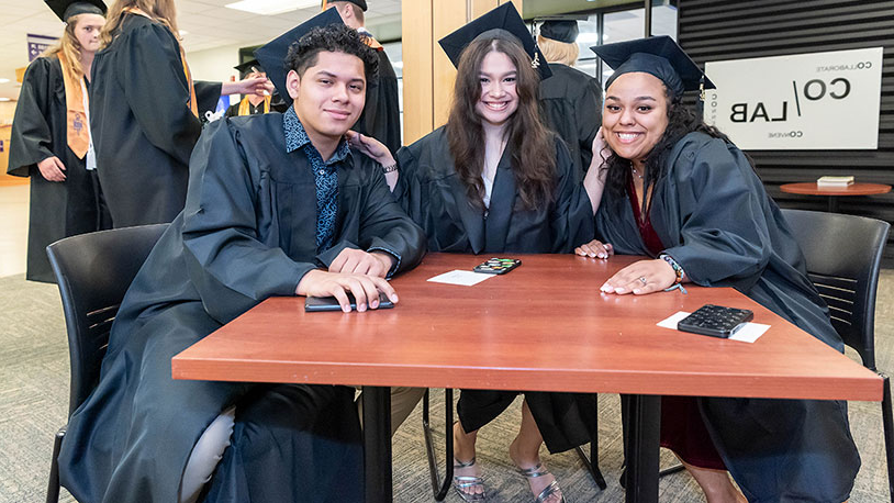 毕业典礼后，三位MCC毕业生微笑着坐在一张桌子旁.