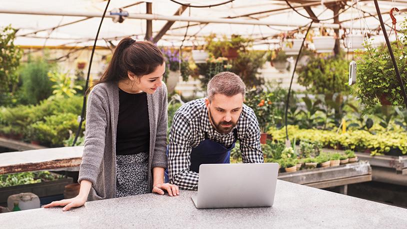 photo of man and woman in greenhouse looking at laptop